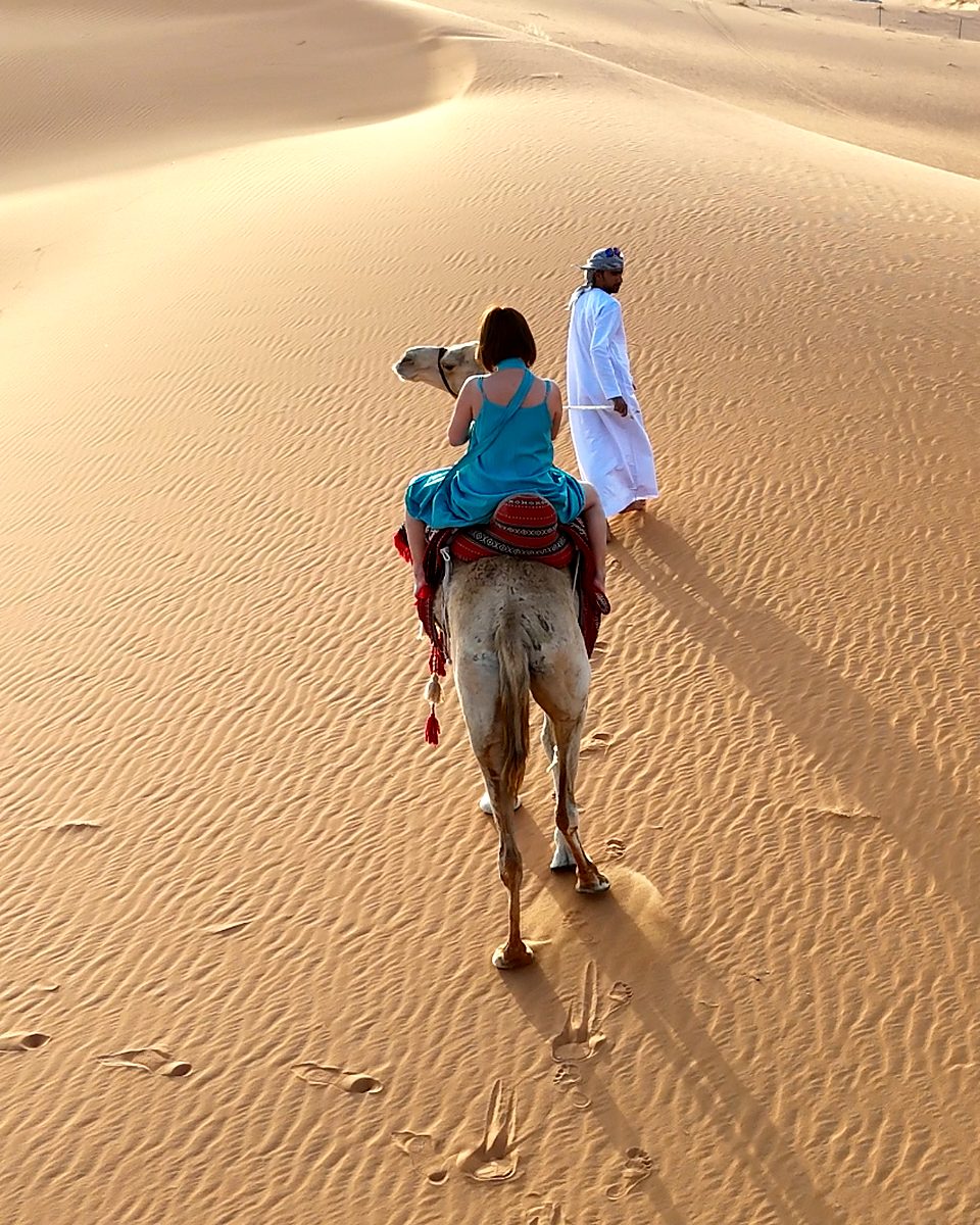 A guest on a camel led by a guide in the late-afternoon sun