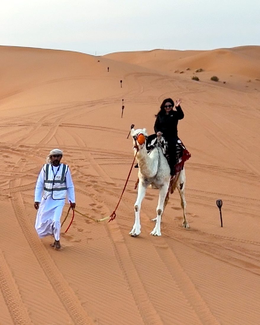 A guide leading a guest on a camel through the dunes near Riyadh