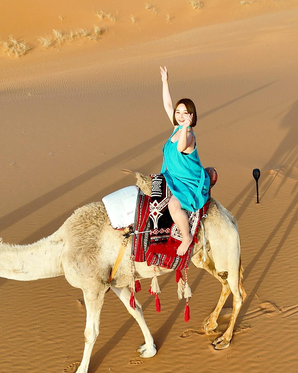 A guest waving from a camel during a desert photo shoot near Riyadh