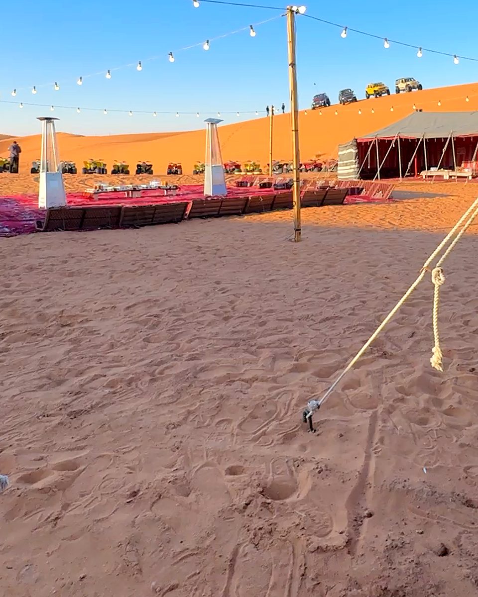 The desert camp seating area with string lights and tents below the dunes