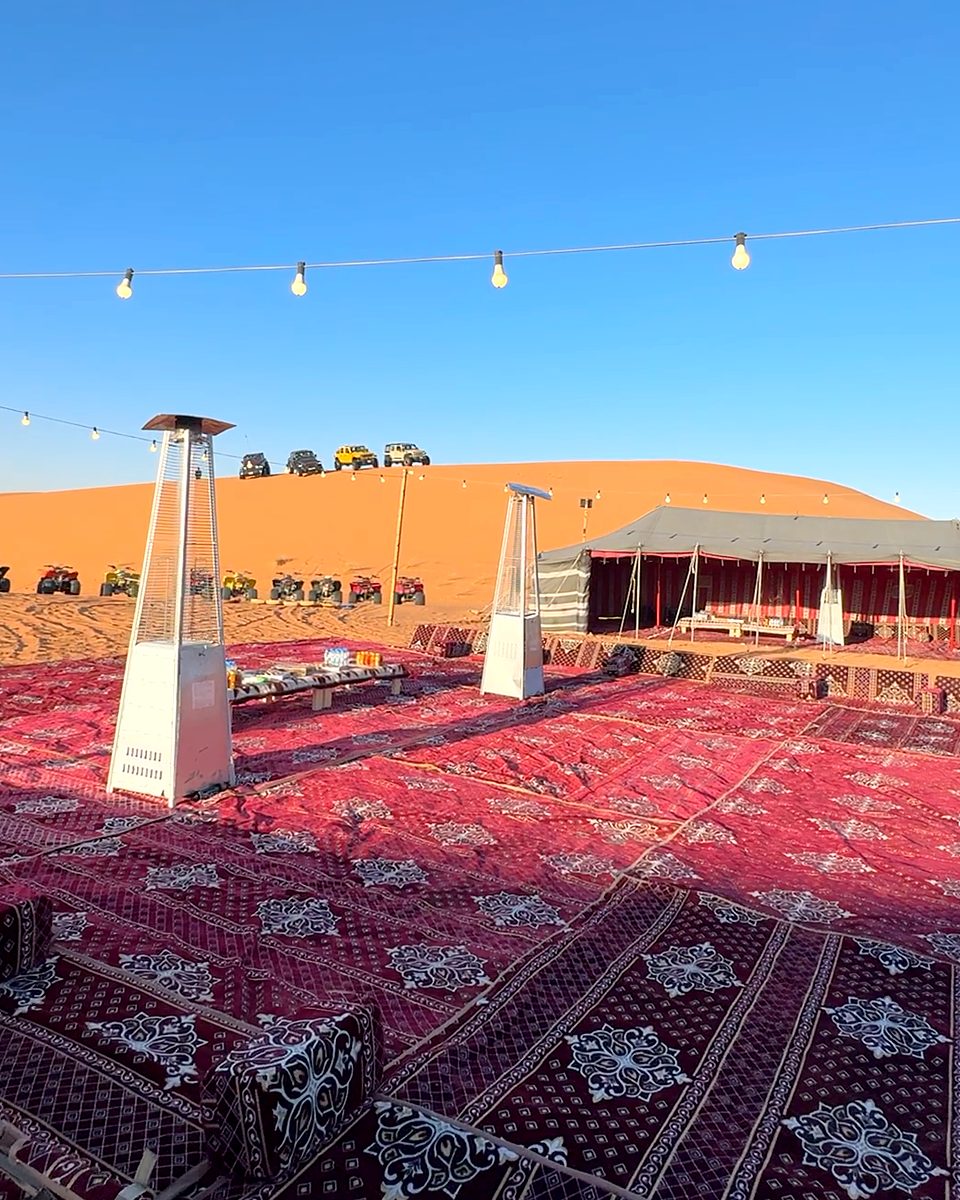 Carpeted majlis seating under string lights beside a traditional tent