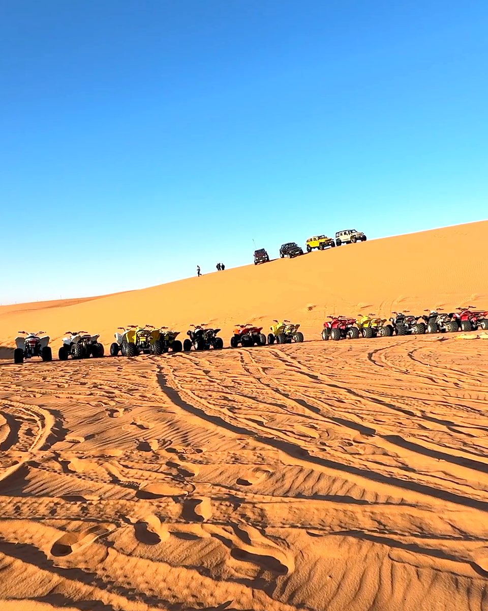 Quad bikes and 4x4s lined up below a dune at the desert camp