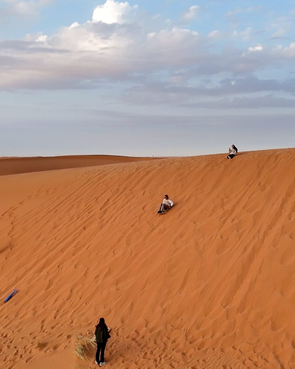 Team members climbing and sandboarding a dune at the Riyadh desert camp