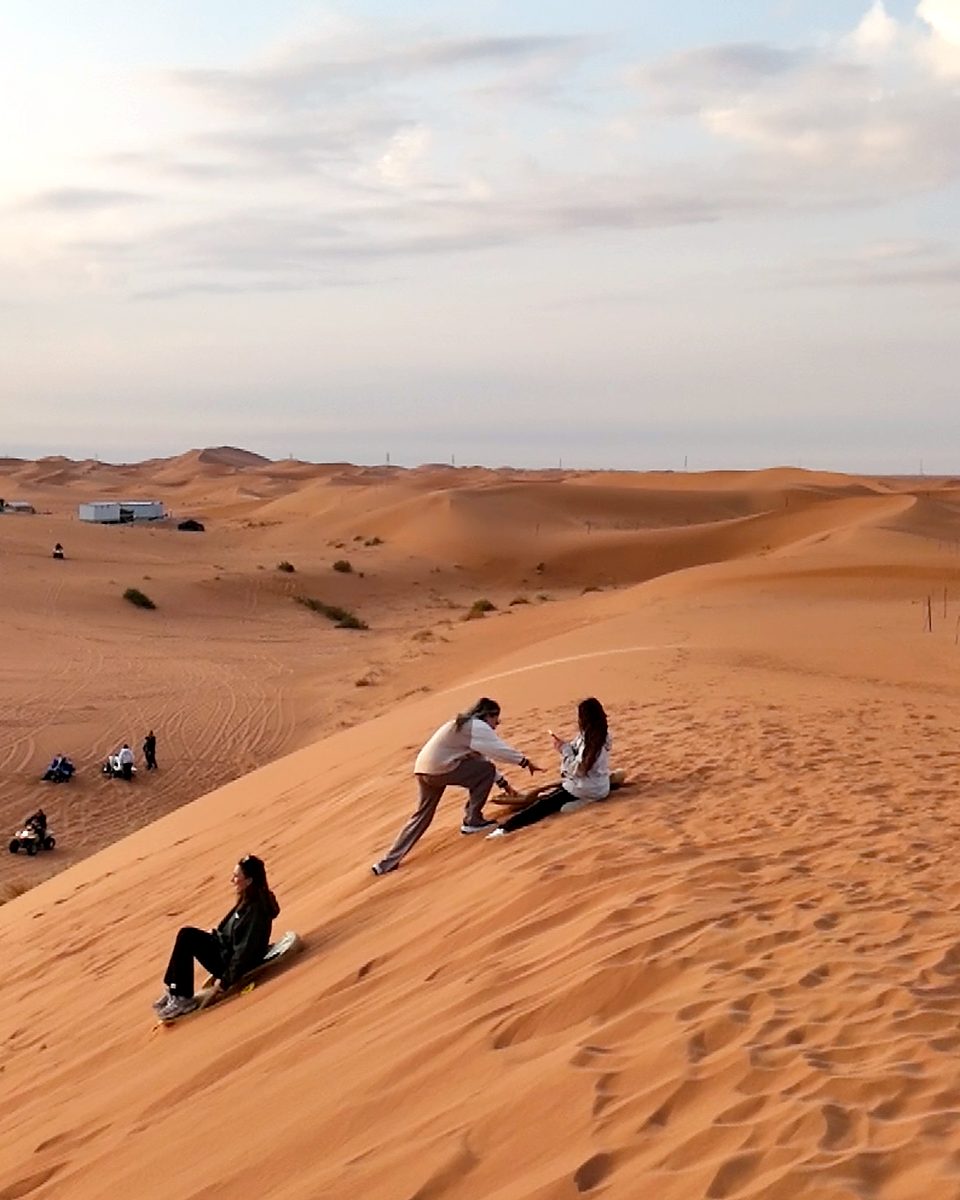 Guests sandboarding down a red dune at the camp east of Riyadh