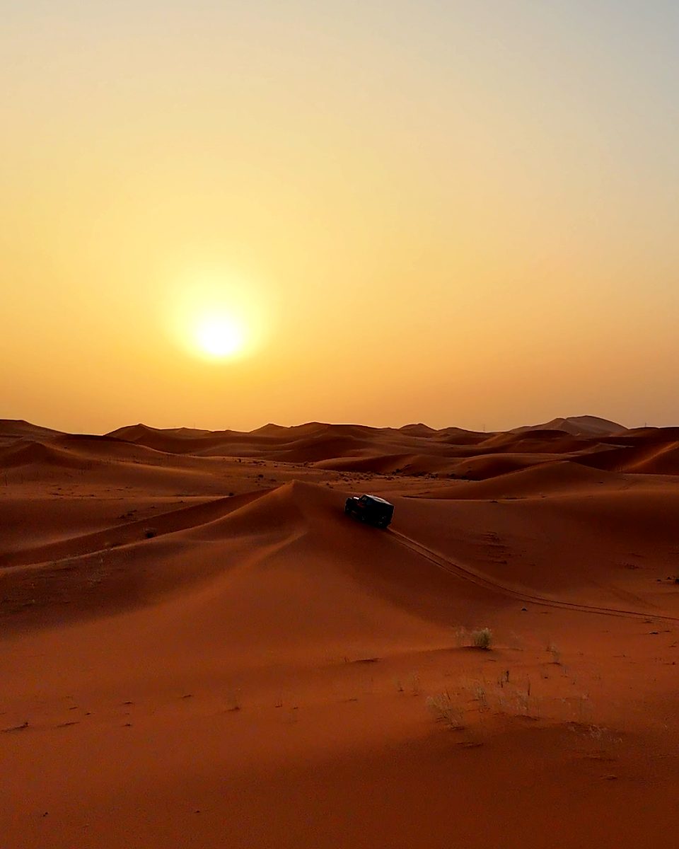 The sun setting over the dunes with a 4x4 below